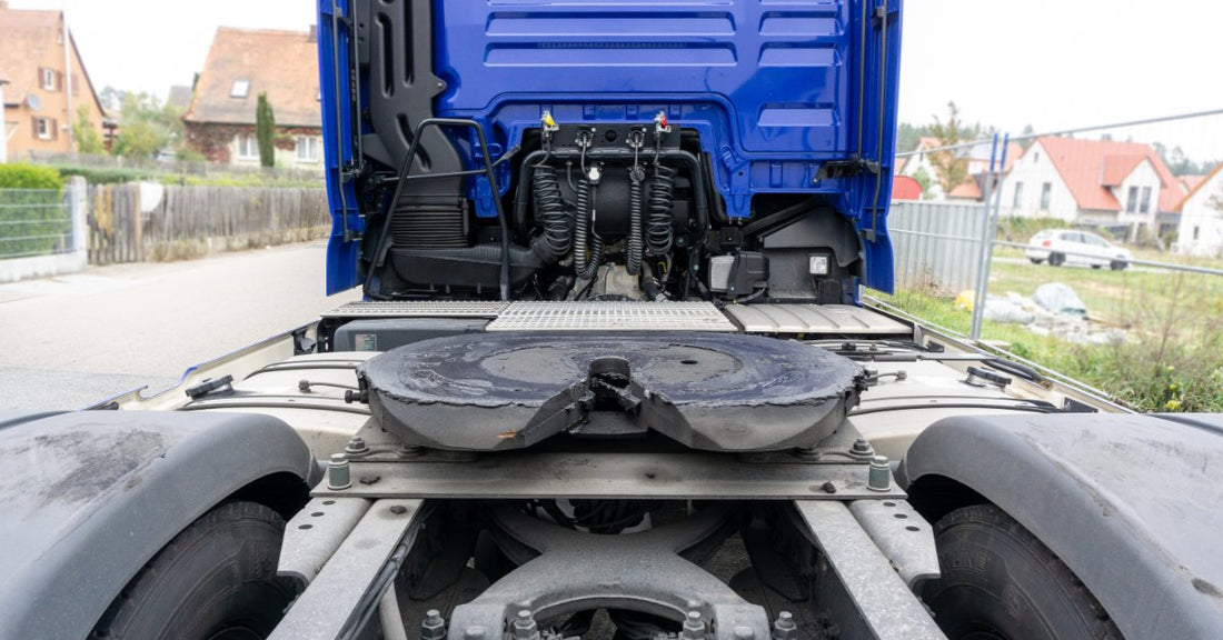A blue cargo truck showing a greased fifth wheel coupling, rear tires, and cab components on a paved road.