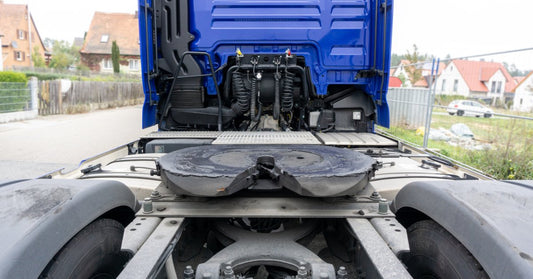 A blue cargo truck showing a greased fifth wheel coupling, rear tires, and cab components on a paved road.
