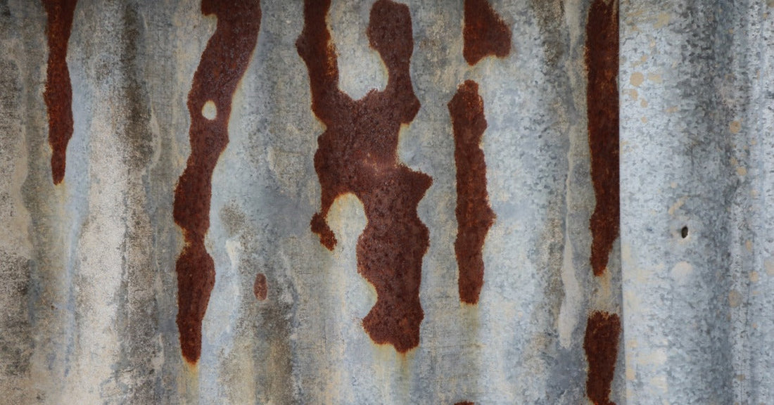 A corrugated gray metal sheet covered with irregular reddish-brown rust patches across its ridged surface.