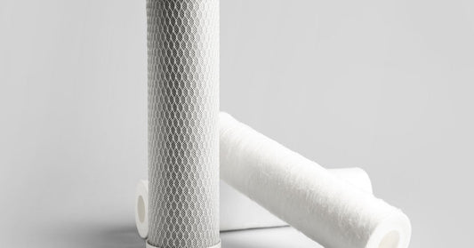 Two white cylindrical filter cartridges standing and lying on a light gray surface with plain background.
