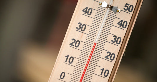 A wooden thermometer with black numbers and red liquid along a glass tube, angled against a blurred background.