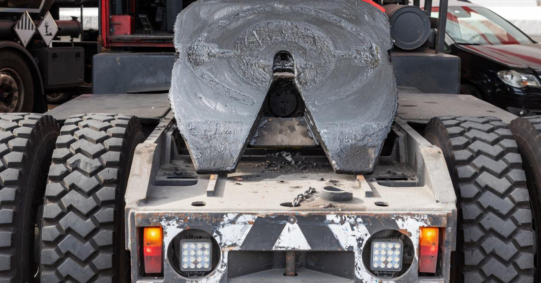 A back view of a red semi-truck without the trailer, giving a clear view of the tilted, fully greased fifth wheel.