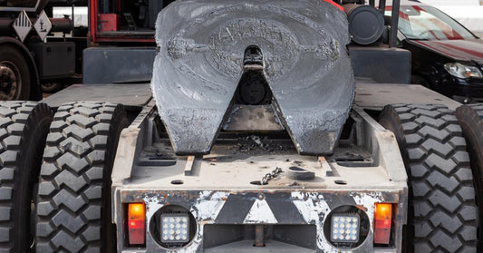 A back view of a red semi-truck without the trailer, giving a clear view of the tilted, fully greased fifth wheel.