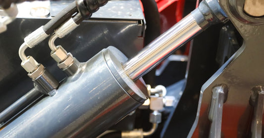 A shiny steel hydraulic cylinder and other components of a hydraulic system all housed within a red casing.