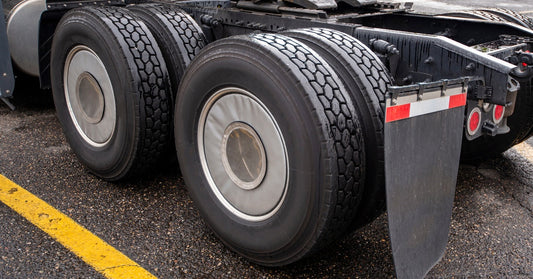 A trailerless semi-truck parked in a parking lot. Its four rear wheels are shielded by metal mud flaps.