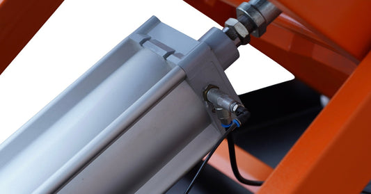 A detailed view of a polished metal hydraulic cylinder installed in a vibrant orange frame and attached to a hose.