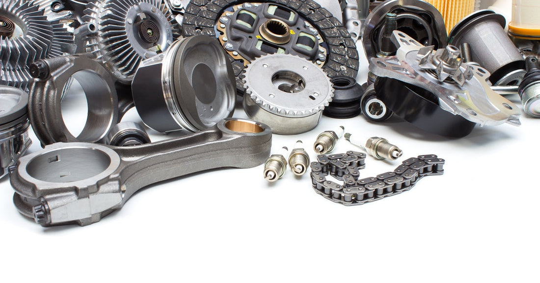 A collection of automotive parts, such as gears, filters, and brake pads, piled together on a white surface.