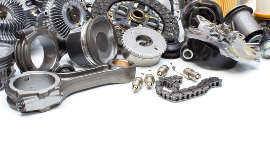 A collection of automotive parts, such as gears, filters, and brake pads, piled together on a white surface.