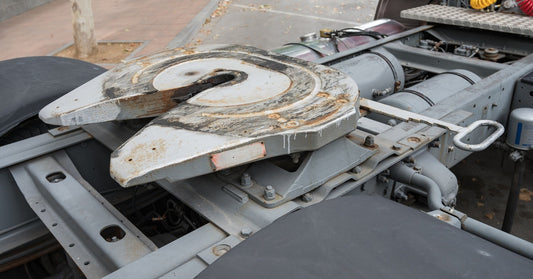 A semi-truck parked in a space near a sidewalk, without a trailer attached, revealing its rusted fifth wheel coupling.