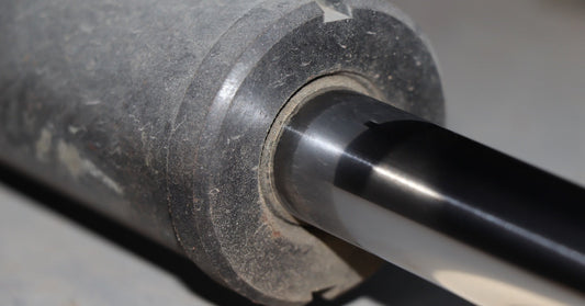 A somewhat dirty hydraulic cylinder, covered in dust and debris, laid out on a smooth, gray surface.