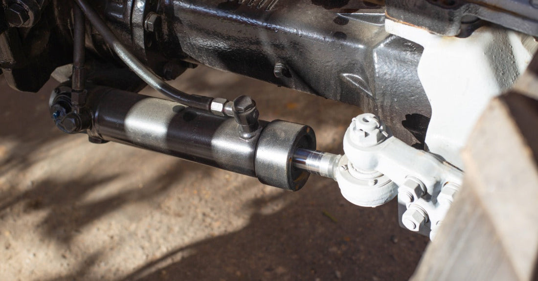 A close up on an exposed part of a vehicle, with a cylinder connected to a piston and several other parts.