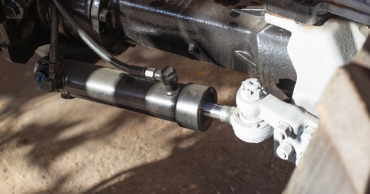 A close up on an exposed part of a vehicle, with a cylinder connected to a piston and several other parts.