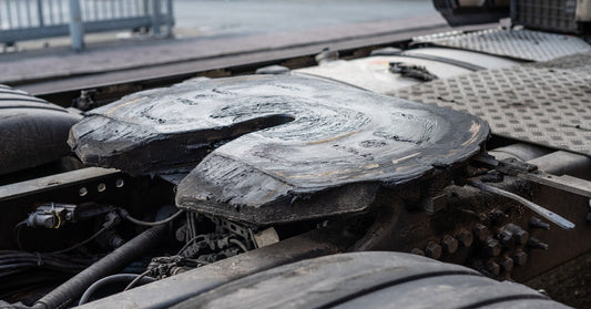 A close-up view of a lubricated fifth wheel hitch on the rear of a semi-truck parked in a construction lot.