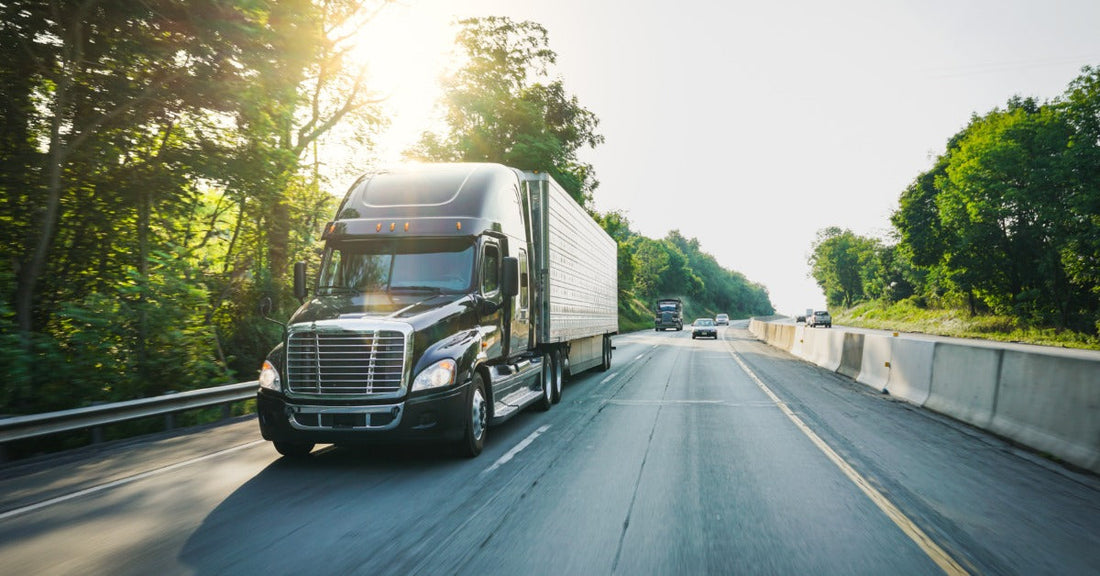 A semi truck with a long trailer driving along a highway carrying freight with motion blur visible along the road.