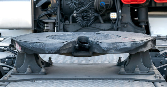 A close view of a fifth wheel hitch on the back of a semi-truck, with the air and electrical connections visible.